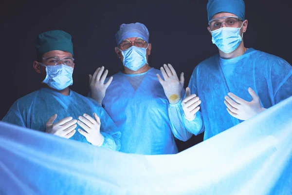 Grupo de cirurgiões no trabalho em sala de operações tonificada em azul. Equipe médica realizando operação — Fotografia de Stock