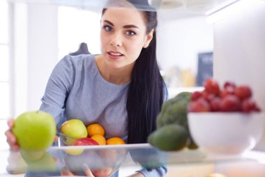 Gülümseyen kadın buzdolabından taze meyve alıyor, sağlıklı yiyecek konsepti.
