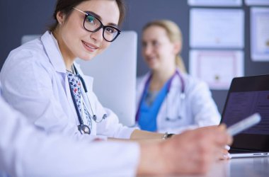 Ciddi bir tıbbi ekip parlak bir ofiste dizüstü bilgisayar kullanıyor.