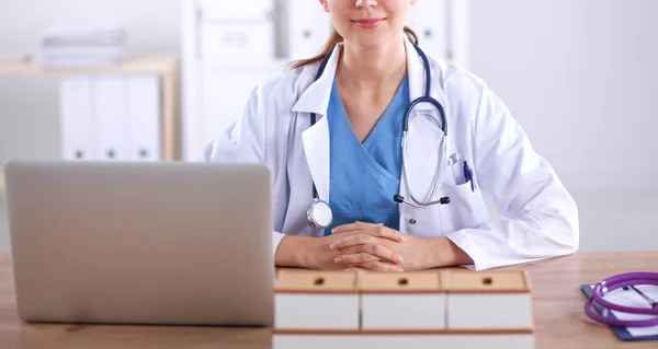 Bela jovem e sorridente médica sentada na mesa e escrevendo. médico feminino — Fotografia de Stock