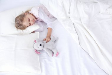 çocuk oyuncak oyuncak ayı ile yatakta uyur küçük kız.