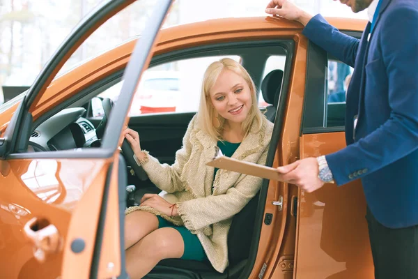 美丽的年轻女子在经销商处选择一辆车时说话帅汽车经销店工人 — 图库照片