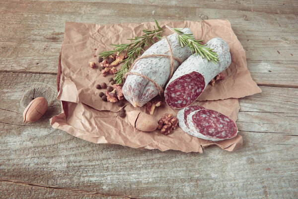 Italian salami wih sea salt, rosemary, garlic and nuts on paper. Rustic style. Top view.