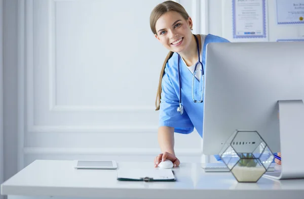 Portrait of female physician using laptop computer while standing near reception desk at clinic or emergency hospital