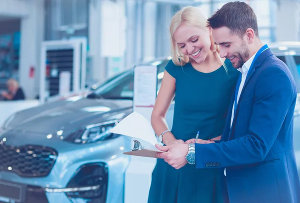 Car salesman sells a car to happy customer in car dealership and hands over the keys