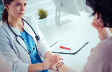 Kadın doktor hastane danışma odasında bir hastayı sakinleştiriyor, elini tutuyor.