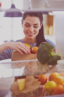 Gülümseyen kadın buzdolabından taze meyve alıyor, sağlıklı yiyecek konsepti.