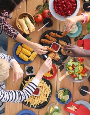Ahşap masada otururken birlikte yemek yiyen bir grup insanın üst düzey görüntüsü. Masada yemek var. İnsanlar fast food yiyor..