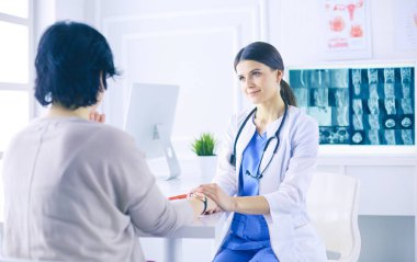 Kadın doktor hastane danışma odasında bir hastayı sakinleştiriyor, elini tutuyor.