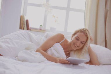 Elinde boş ekranlı dijital tablet tutan ve yatak odasında kameraya gülümseyen bir kız.