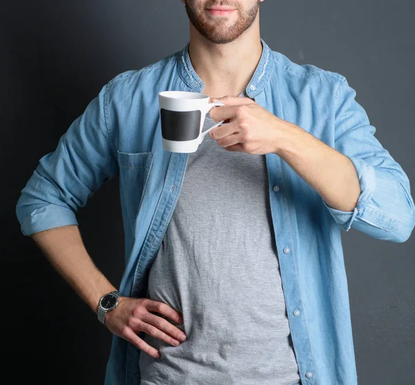 Portret van een knappe jongeman permanent en houden van een kopje koffie in zijn handen — Stockfoto