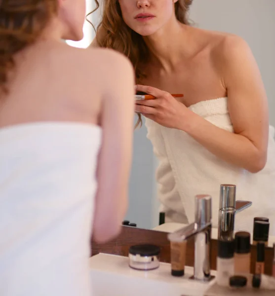 Young woman looking in the mirror and putting make-up on. — Stock Photo, Image