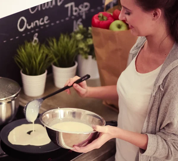 Young woman prepares pancakes in the kitchen while standing near the table. Woman in the kitchen. Cooking at kitchen. — Stock Photo, Image