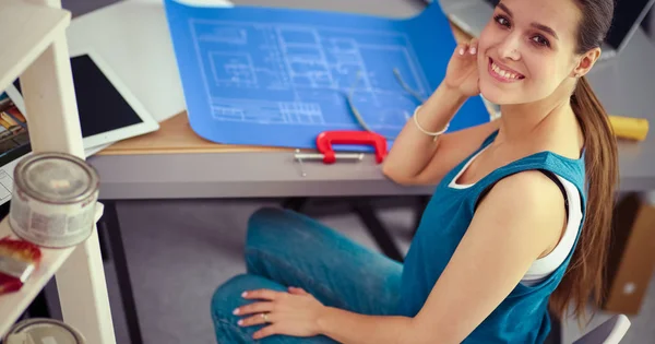 Jeune femme assise au bureau avec instruments, plan et ordinateur portable — Photo