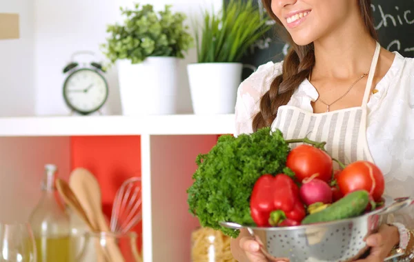 Mujer joven sonriente sosteniendo verduras de pie en la cocina. Jovencita sonriente —  Fotos de Stock