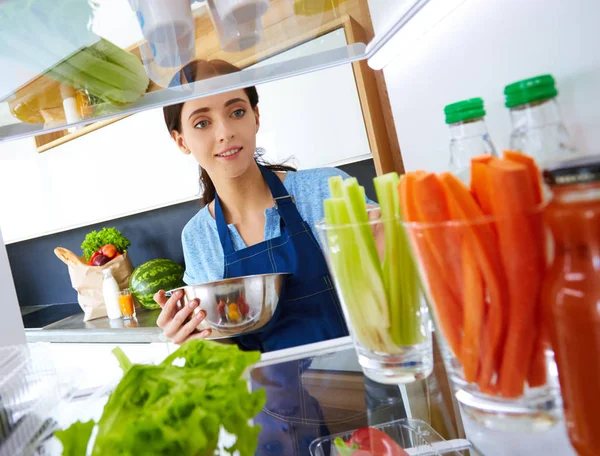 Portrait of female standing near open fridge full of healthy food, vegetables and fruits. Portrait of female — Stock Photo, Image