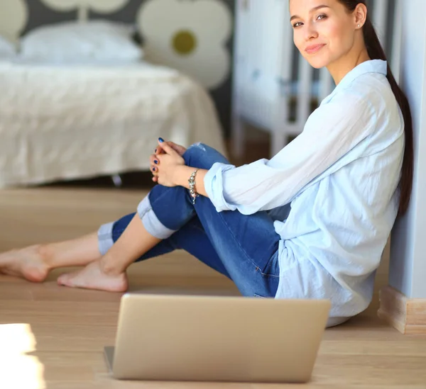 Ung kvinna som sitter på golvet nära barnens babysäng med laptop. Ung mamma — Stockfoto