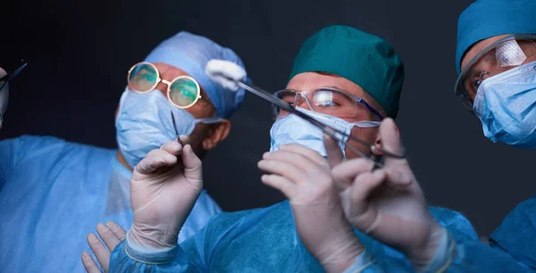 Grupo de cirurgiões no trabalho em sala de operações tonificada em azul. Equipe médica realizando operação — Fotografia de Stock