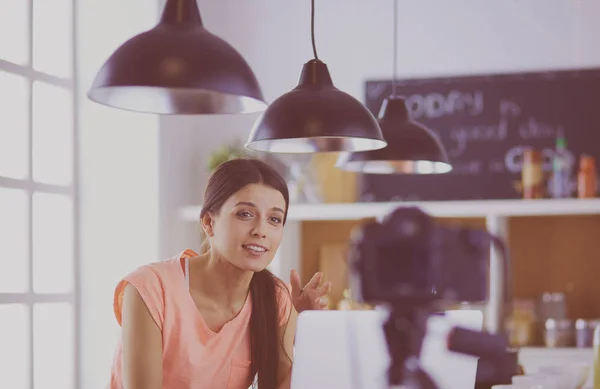 Mujer joven en la cocina con computadora portátil buscando recetas, sonriendo. Concepto de bloguero de alimentos — Foto de Stock