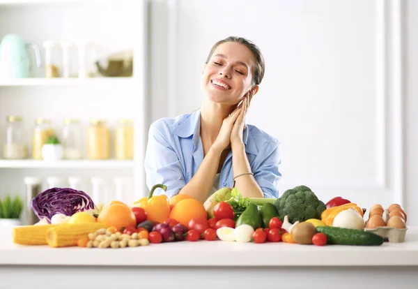 Jeune et mignonne femme assise à la table pleine de fruits et légumes à l'intérieur en bois. — Photo