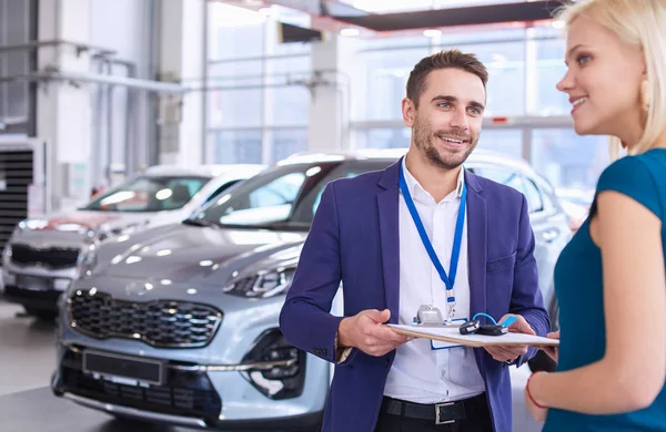 Car salesman sells a car to happy customer in car dealership and hands over the keys