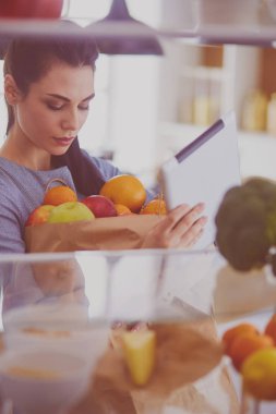 Gülümseyen kadın buzdolabından taze meyve alıyor, sağlıklı yiyecek konsepti.