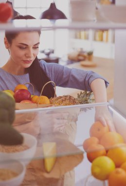 Gülümseyen kadın buzdolabından taze meyve alıyor, sağlıklı yiyecek konsepti.