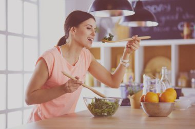 Gülümseyen genç kadın mutfakta taze salata karıştırıyor..