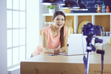 Mutfakta dizüstü bilgisayara benzeyen tariflerle gülümseyen genç bir kadın. Gıda blogcusu kavramı