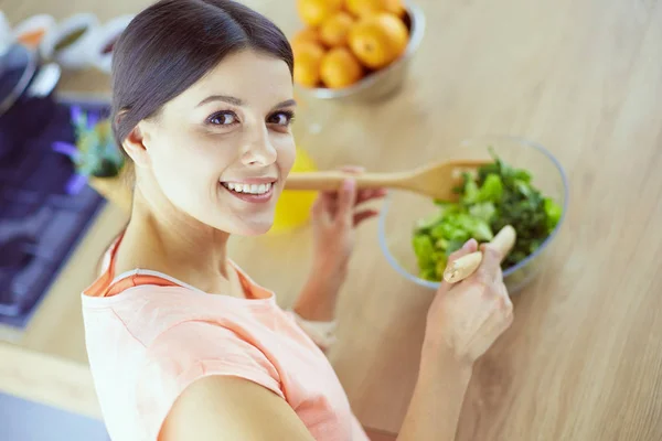 Glimlachende jonge vrouw mengen van verse salade in de keuken. — Stockfoto