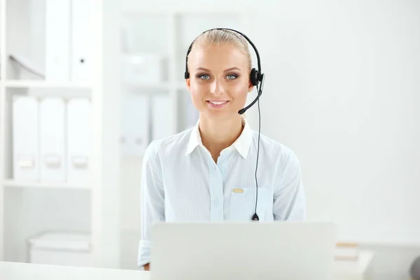 Portrait of pretty young female operator sitting at office desk with headset — Stock Photo, Image