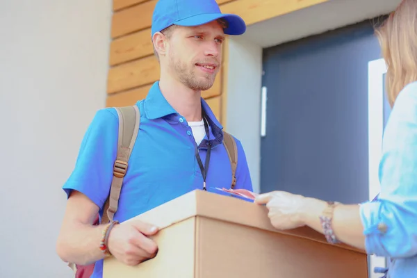 Uomo di consegna sorridente in uniforme blu che consegna pacchi al destinatario concetto di servizio di corriere. Uomo sorridente consegna in uniforme blu — Foto Stock