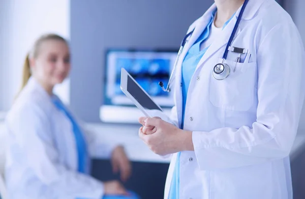 Inyección del médico sosteniendo pastillas y un vaso de agua en la clínica con su colega en el fondo. —  Fotos de Stock