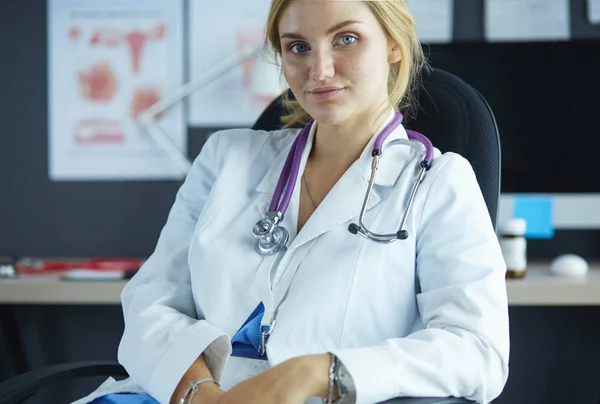 Mooie jonge glimlachende vrouwelijke arts zittend aan het bureau — Stockfoto