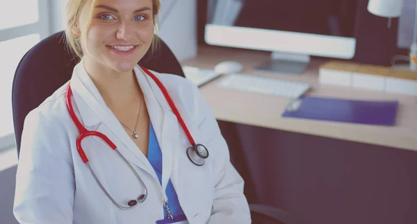 Zelfverzekerde vrouwelijke arts zit aan het bureau en glimlacht naar de camera — Stockfoto