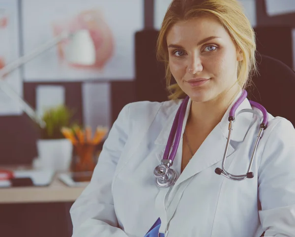 Όμορφη νεαρή χαμογελαστή γυναίκα γιατρός κάθεται στο γραφείο — Φωτογραφία Αρχείου
