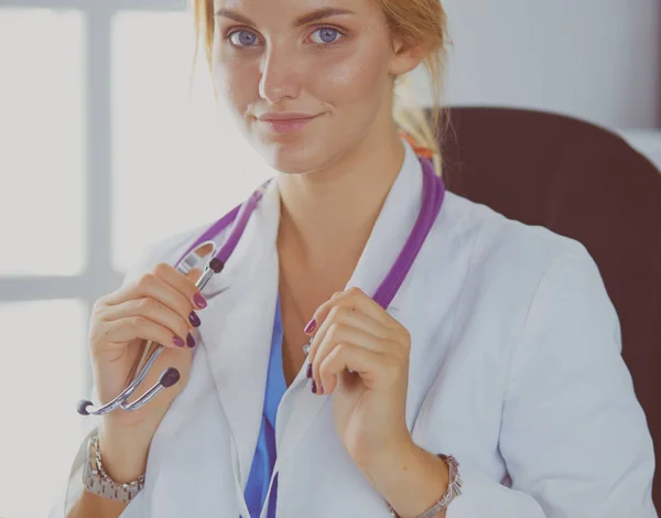Mooie jonge glimlachende vrouwelijke arts zittend aan het bureau — Stockfoto
