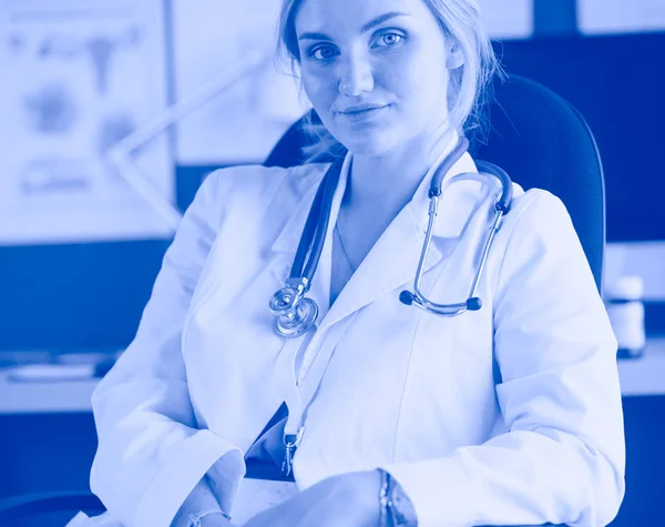 Beautiful young smiling female doctor sitting at the desk — Stock Photo, Image