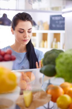 Gülümseyen kadın buzdolabından taze meyve alıyor, sağlıklı yiyecek konsepti.
