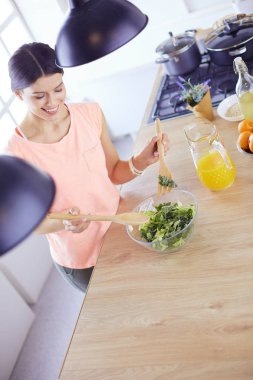 Gülümseyen genç kadın mutfakta taze salata karıştırıyor..