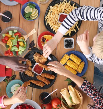 Ahşap masada otururken birlikte yemek yiyen bir grup insanın üst düzey görüntüsü. Masada yemek var. İnsanlar fast food yiyor..