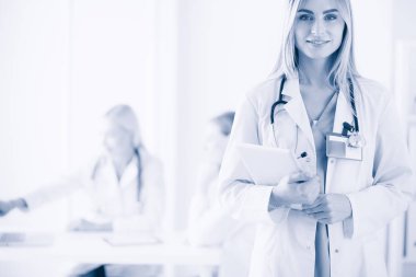 Genç bir kadın doktorun portresi, elinde aipad ile, bir tıp ofisinde.