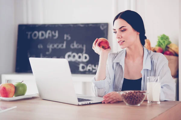 Donna con mela e laptop seduta in cucina — Foto Stock