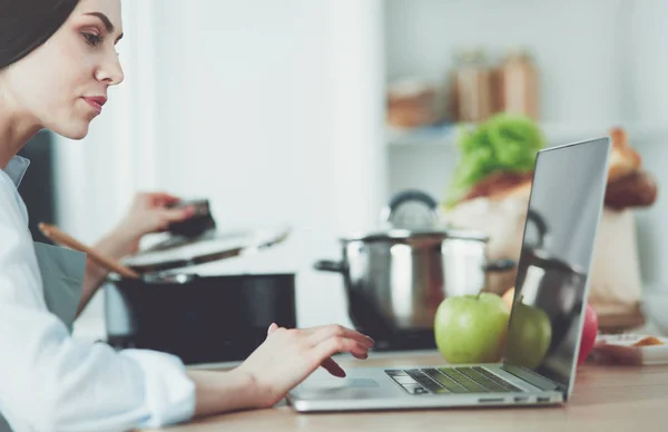 Giovane donna in cucina con computer portatile alla ricerca di ricette, sorridente. Concetto di food blogger — Foto Stock