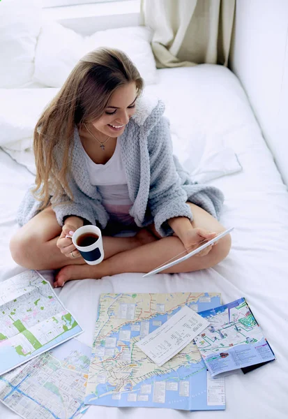 Mujer joven y relajada sentada en la cama con una taza de café y una tableta digital —  Fotos de Stock