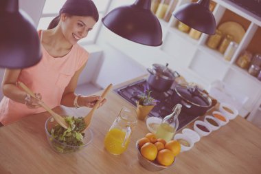 Gülümseyen genç kadın mutfakta taze salata karıştırıyor..
