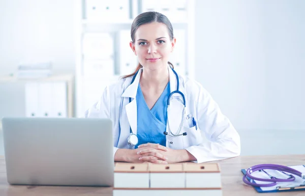 Bela jovem e sorridente médica sentada na mesa e escrevendo. médico feminino — Fotografia de Stock