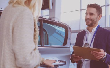 Kadın satıcısı galeride yeni bir arabanın yanında duruyor.