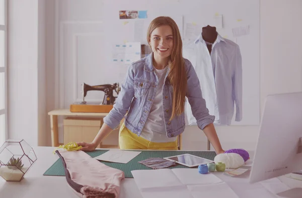 Schöne Modedesignerin steht neben Schreibtisch im Atelier — Stockfoto