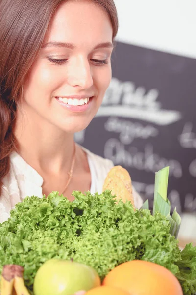 Mujer joven sonriente sosteniendo verduras de pie en la cocina. Jovencita sonriente —  Fotos de Stock